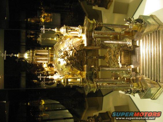 Ornate golden reliquary with intricate carvings and crosses, reflected in a mirrored surface