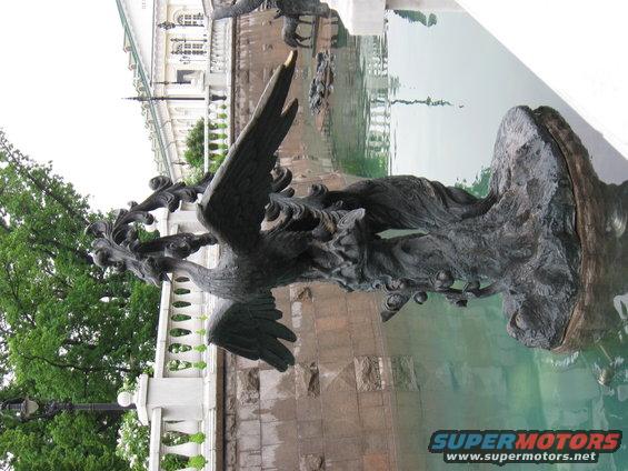 Bronze eagle sculpture with outstretched wings in a fountain, with a building and trees in the background