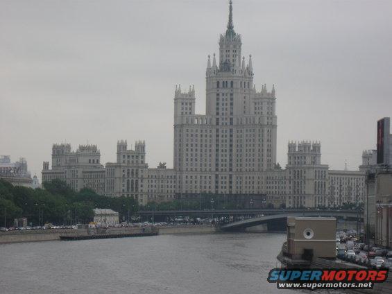 Big white building by a river with a bridge and some cars