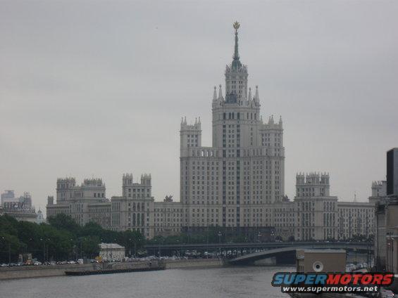 Tall white building with spire, bridge over river, and cars on road