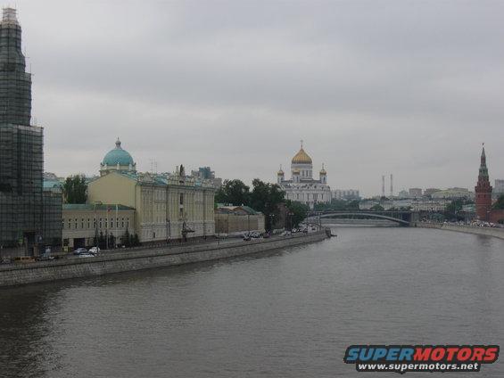 Cityscape with river, bridge, and domed buildings under a cloudy sky