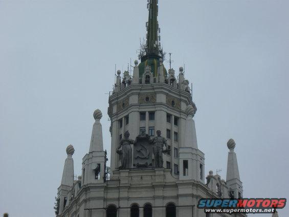 Building spire with statues and Soviet emblem against a cloudy sky