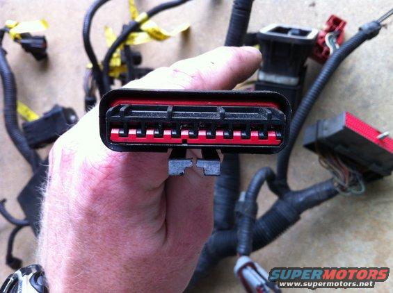 Wiring harness connector with red and black housing, held by a hand
