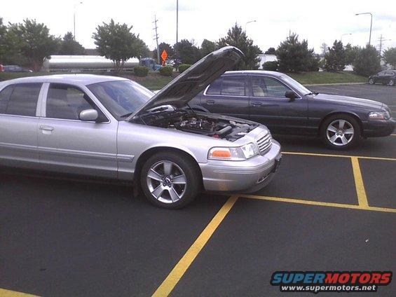 Silver 2003 Ford Crown Victoria with hood open, parked next to a dark gray 2003 Ford Crown Victoria