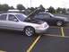 2003 Ford Crown Victoria - Two Ford Crown Victorias are parked in a lot, one with its hood up, revealing the engine.