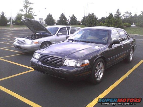 Two Ford Crown Victorias parked in a lot, one with the hood open