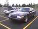 2003 Ford Crown Victoria - A dark-colored Ford Crown Victoria is parked in front of a silver one with its hood up.