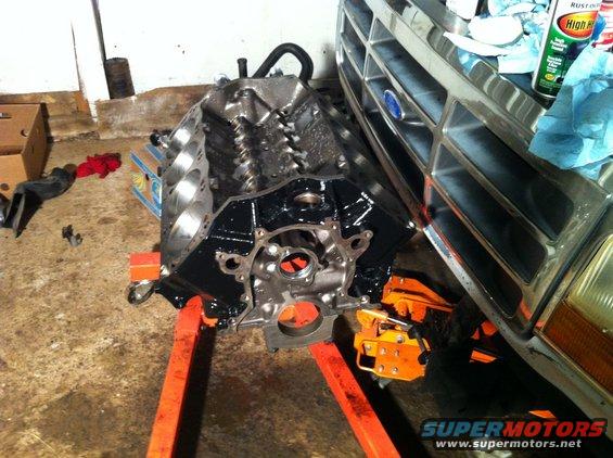 Engine block on an orange stand, next to the front grille of a Ford truck. Some cleaning supplies are on the grille