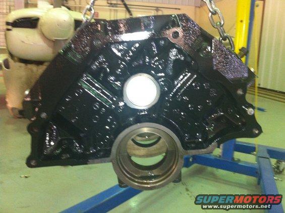 Black engine block with oil residue, suspended by chains, with a blue stand visible