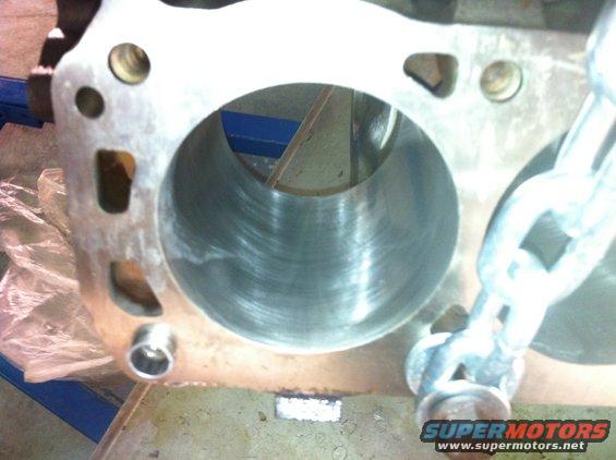 Engine cylinder block with visible honing marks inside the cylinder bore and a metal chain attached