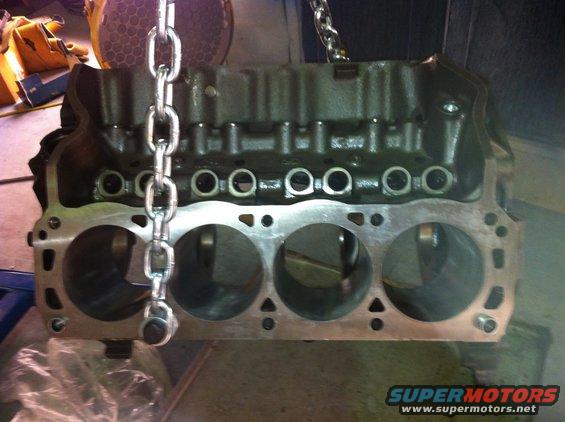 engine block with chain hoist attached, showing cylinder bores