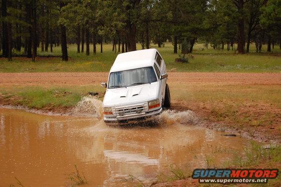 White SUV driving through muddy water, front view, hood scoops visible