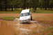 1996 Ford Bronco - A white SUV navigates a muddy puddle in a wooded area.