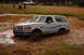 1996 Ford Bronco - White 1996 Ford Bronco navigates a muddy obstacle course, with spectators in the background.