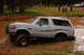 1996 Ford Bronco - White 1996 Ford Bronco navigating a muddy off-road course with spectators nearby.