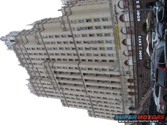 Tall building with many windows and parked cars on the right side