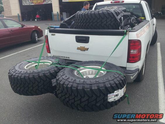White pickup truck bed loaded with large off-road tires, two secured to the rear bumper