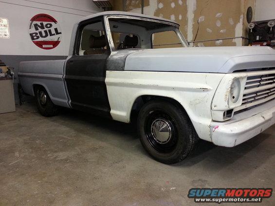 1967 Ford F-100 pickup truck in primer, undergoing restoration. The truck has a two-tone paint scheme with black doors and grey/white body panels