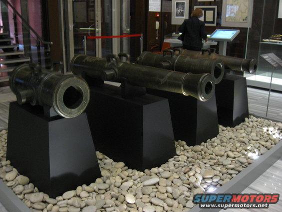 Three antique cannons displayed on black pedestals with white stones
