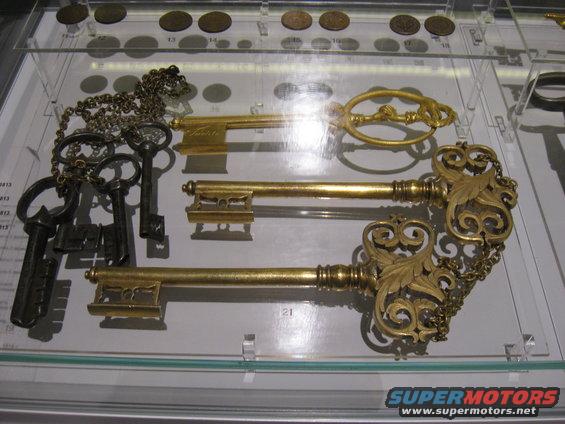 Display of old keys, some ornate gold, others dark metal, with coins above