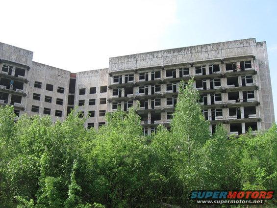 Abandoned concrete building with many empty window frames, surrounded by green trees