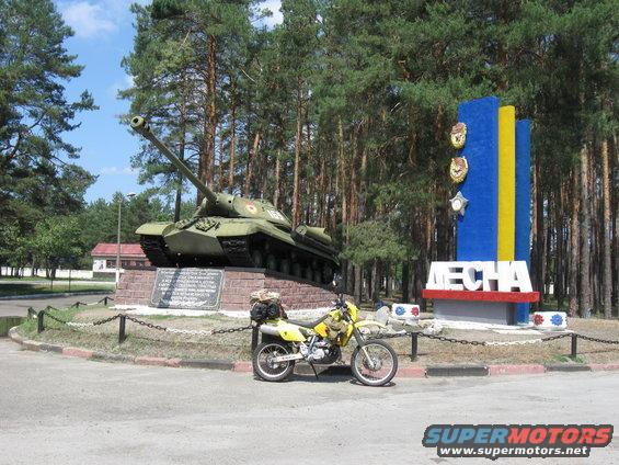 Yellow dual-sport motorcycle parked by tank monument