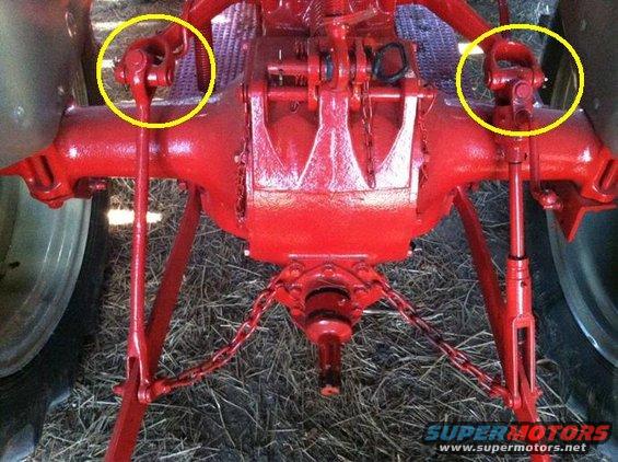 Close-up of a red tractor's rear axle with yellow circles highlighting the PTO shafts