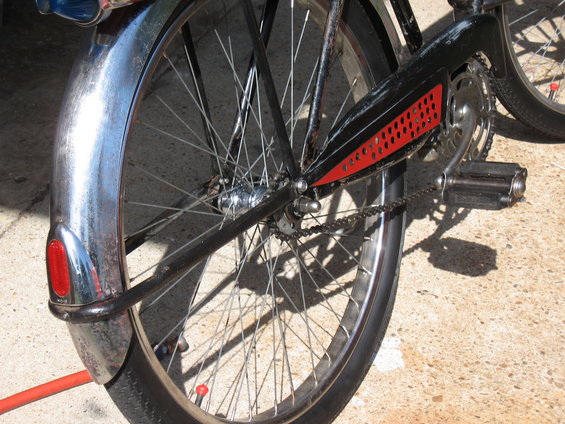 Bicycle rear wheel with chrome fender and red reflector, black chain guard with red perforated insert