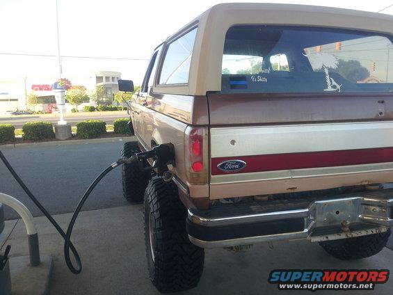 1988 Ford Bronco with large tires refueling at a gas station, rear view