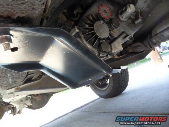 Underside of a vehicle showing the transmission and a skid plate, with a tire visible