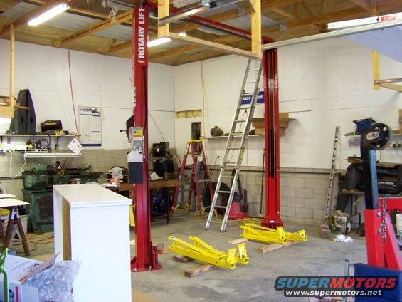 Garage with red rotary lift, yellow lift arms, ladders, and tools