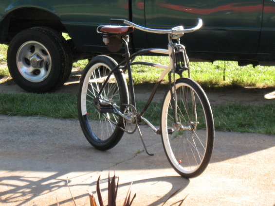 Cruiser bicycle with white rims and red saddle, parked next to a green truck