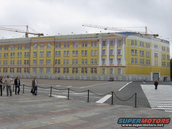 Yellow building under construction with cranes overhead, people walking in foreground