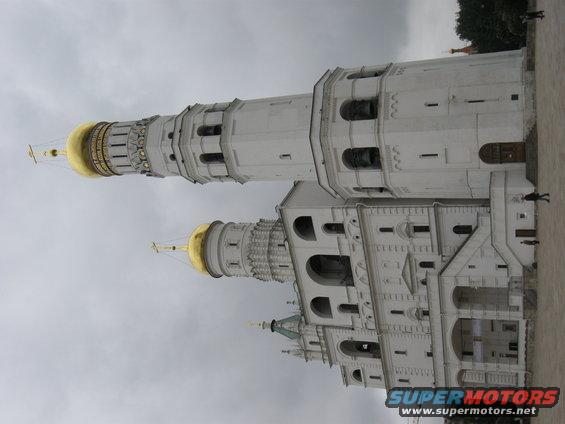 White bell towers with golden domes under a cloudy sky, with a watermark at the bottom right