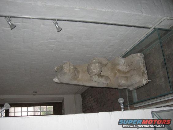 Stone sculpture of a reclining animal mounted on a ceiling, with spotlights above