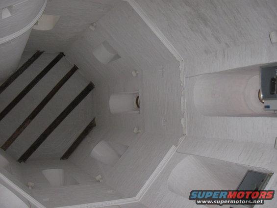 Interior of a white, octagonal structure with dark beams and white cylindrical protrusions. A metal box is mounted on the wall