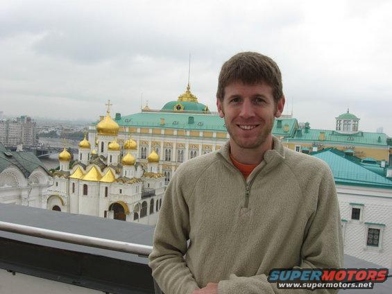 Man smiling in front of golden-domed buildings and green roofs of the Kremlin