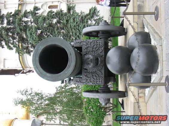 Close-up of an old cannon with ornate carvings and cannonballs nearby