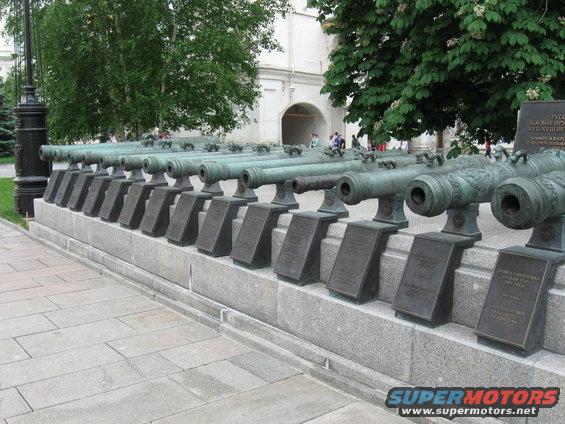 Row of old cannons on display in front of a building with trees