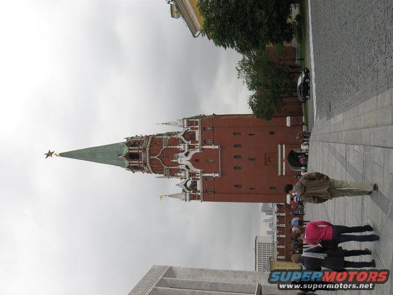 Kremlin tower with a star on top, people walking on a cobblestone path, and a black car in the background