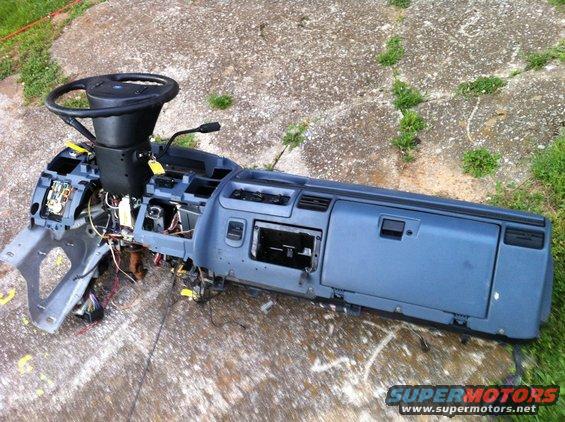 Disassembled dashboard with steering wheel and wiring, lying on concrete