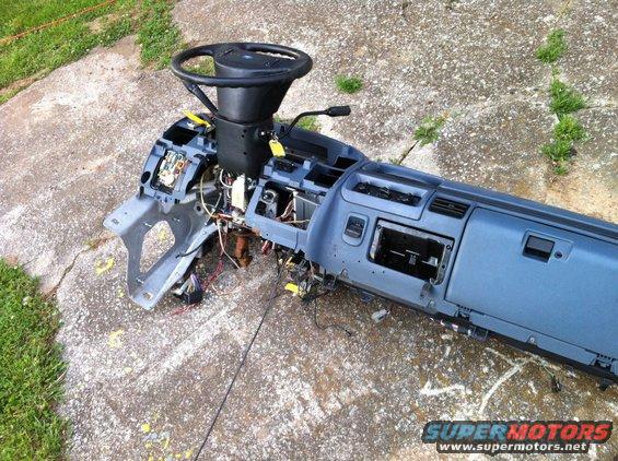 Disassembled blue dashboard assembly with steering wheel and wiring, lying on concrete