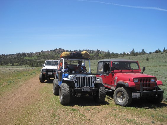 Red Jeep Wrangler and two other off-road vehicles parked on a dirt road