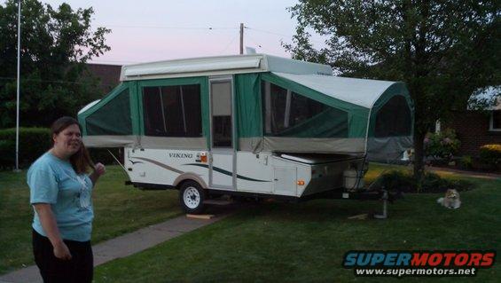 Pop-up camper with green canvas and white body, a woman stands to the left