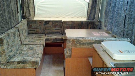 Interior of a pop-up camper with U-shaped seating, a table, and a sink area