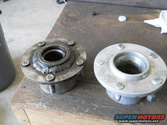 Two metal wheel hubs on a wooden surface; one appears used with weld marks, the other is clean