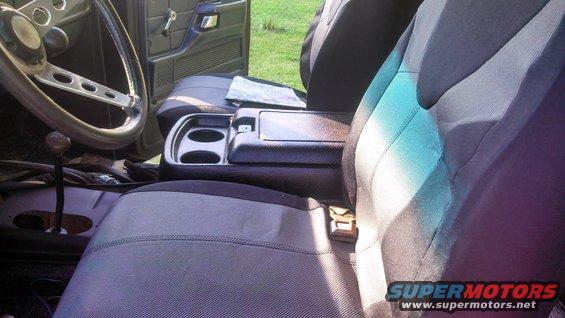 Interior view of a vehicle, showing the steering wheel, dashboard, center console with cup holders, and seats