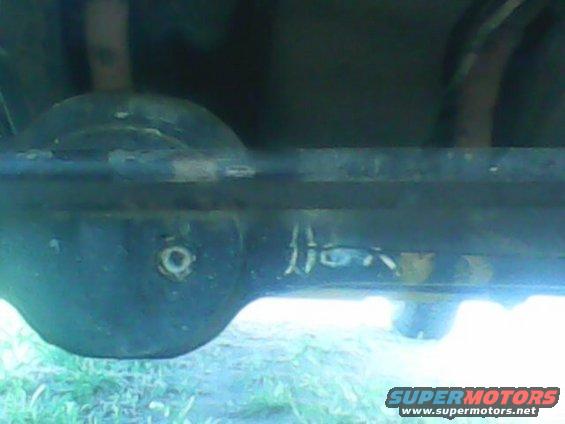 Underside view of a vehicle's rear axle and suspension components, showing rust and wear