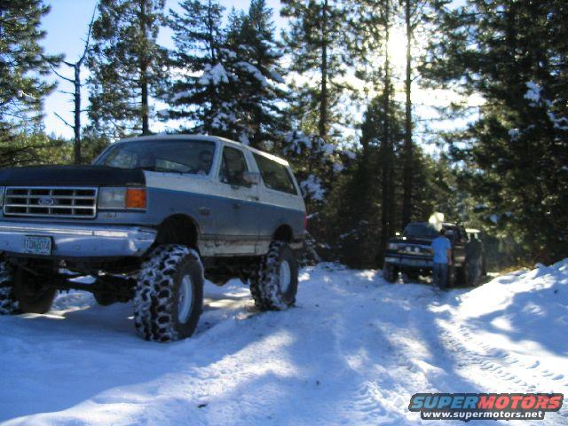 Modified Ford Bronco with large tires in snow, another truck behind it