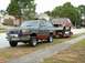 1979 Ford Bronco - A gray Ford Bronco tows a red Ford Bronco on a trailer down a suburban street.